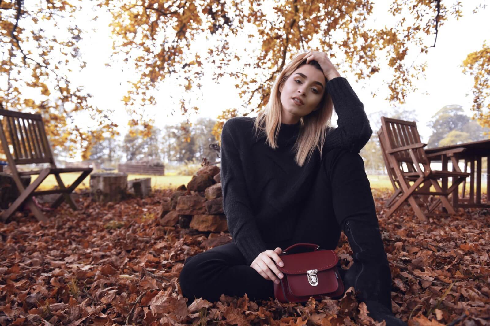 Woman sat on the grass with a Luna bag in Oxblood Red