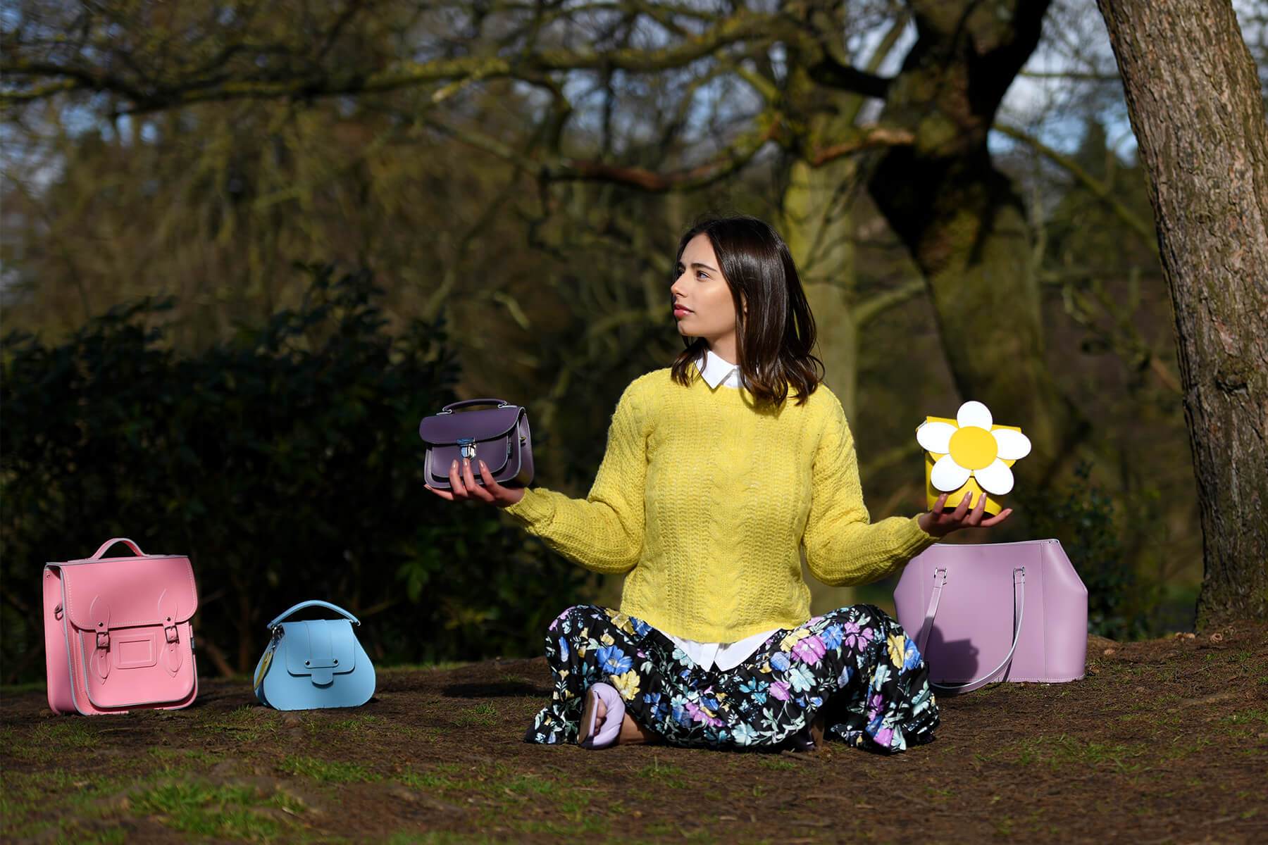 Woman Sat On Grass Surrounded By Colourful Zatchels Bags