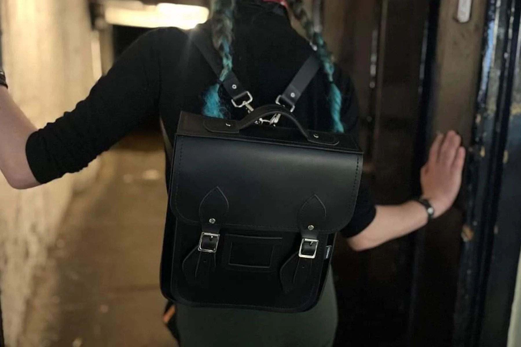 person wearing black leather satchel backpack