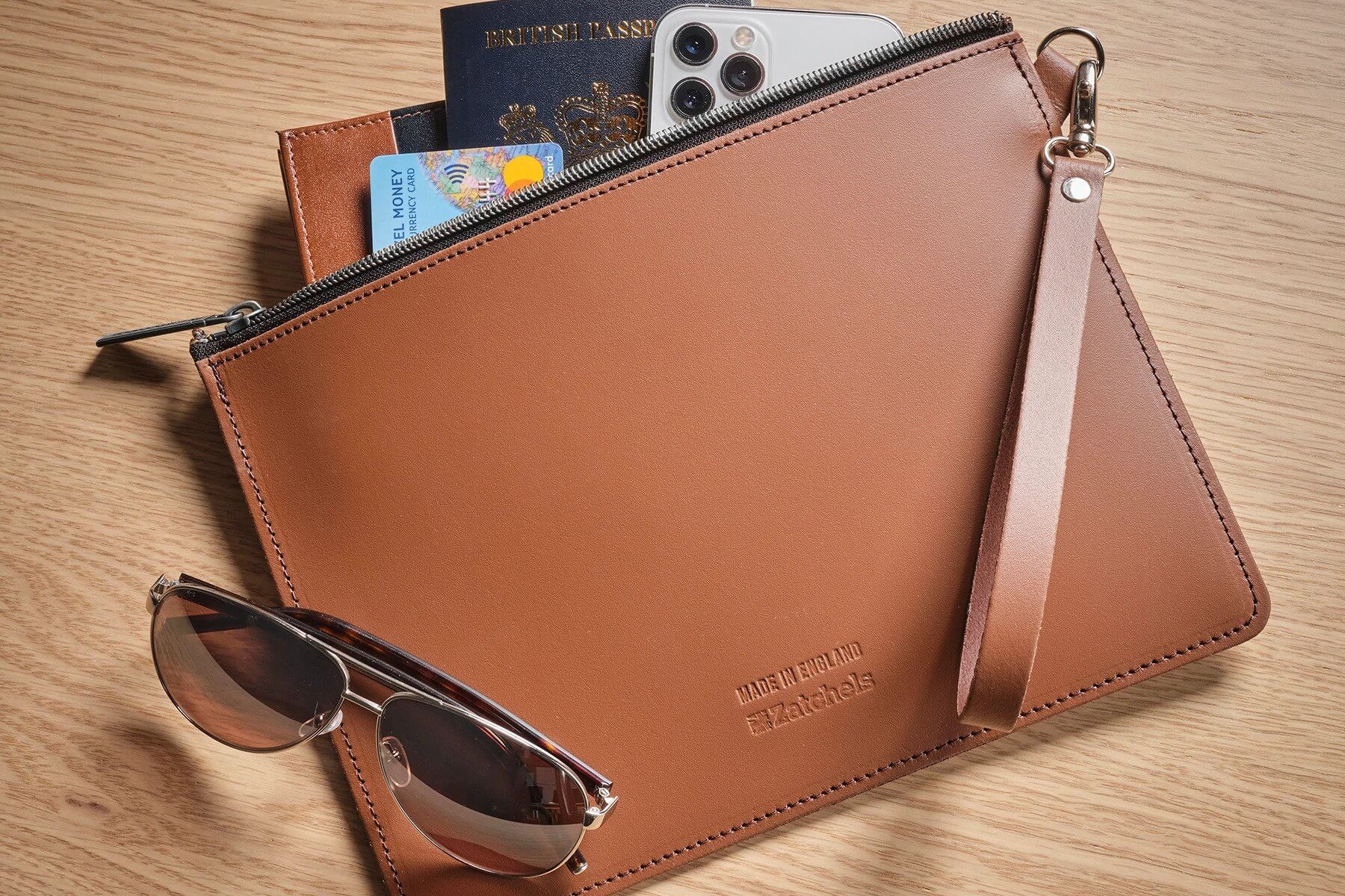 leather folio case in brown containing travel essentials and sunglasses placed on top