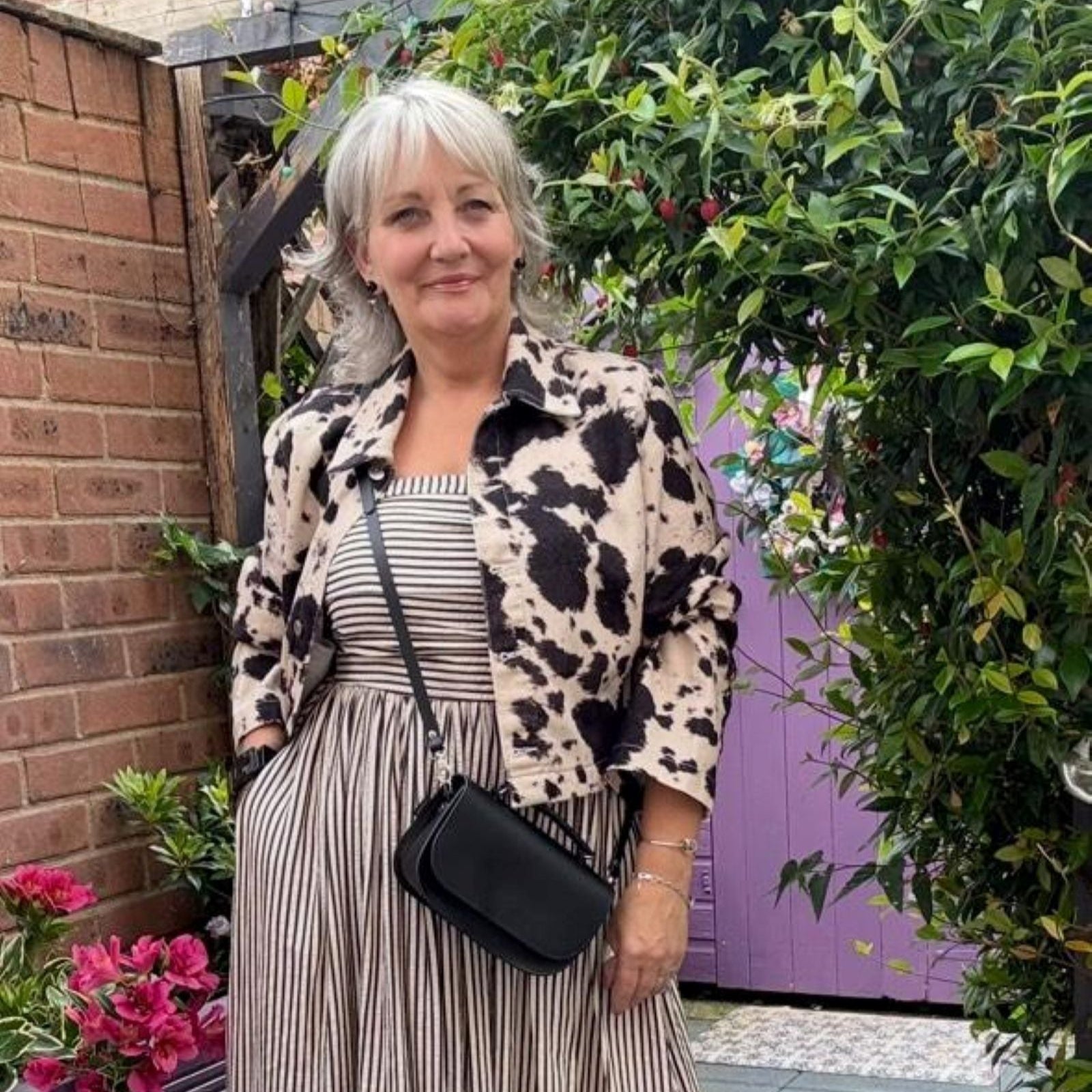 Woman in a patterned outfit standing outdoors with plants and flowers in the background