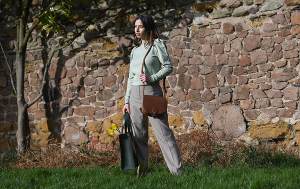 Woman in Beige standing by a wall holding a back tote bag