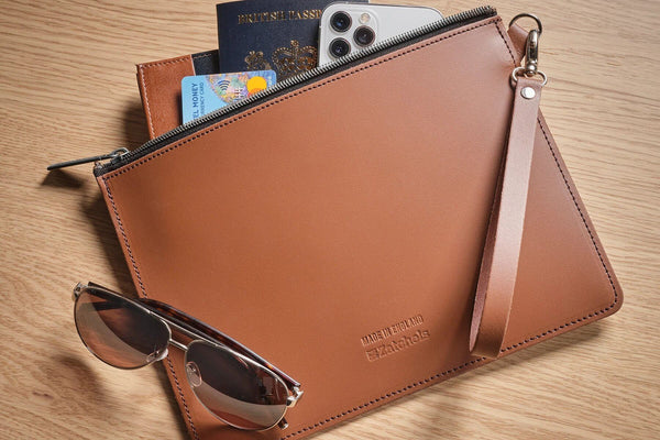 leather folio case in brown containing travel essentials and sunglasses placed on top