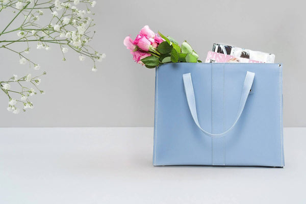 Handmade Leather Shopper in pastel blue filled with flowers and magazines on a white table next to a flower