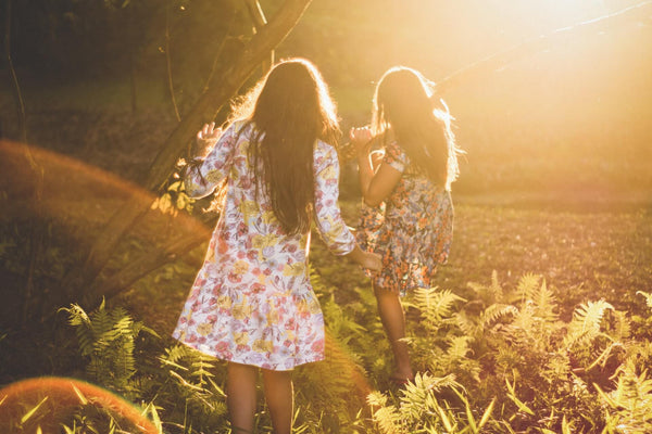 two women wearing patterned dresses walking through a meadow at sunset